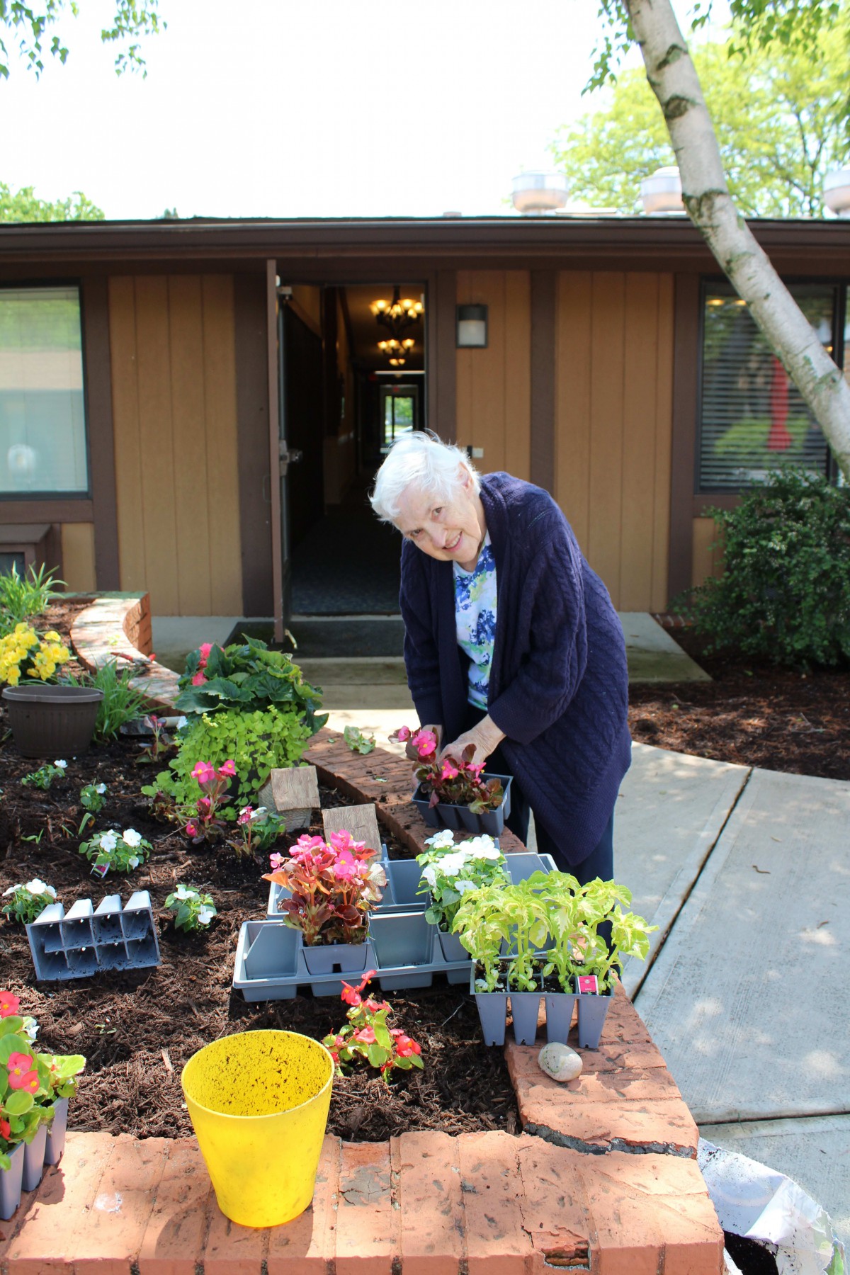 An elderly woman engaging in gardening activities outside her home.