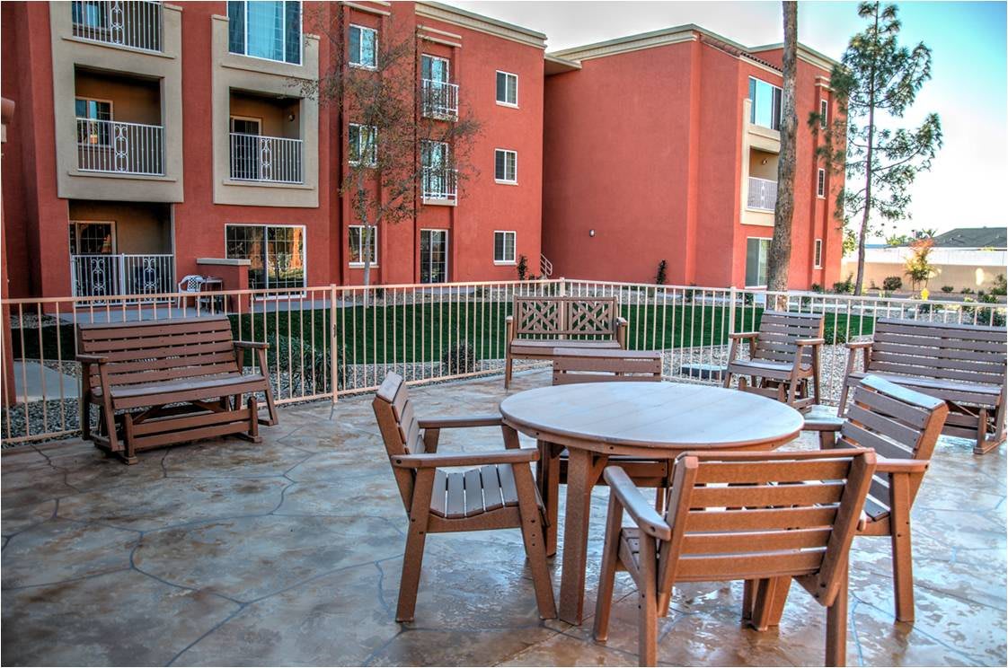 A patio area with wooden furniture, overlooking a brick apartment complex.