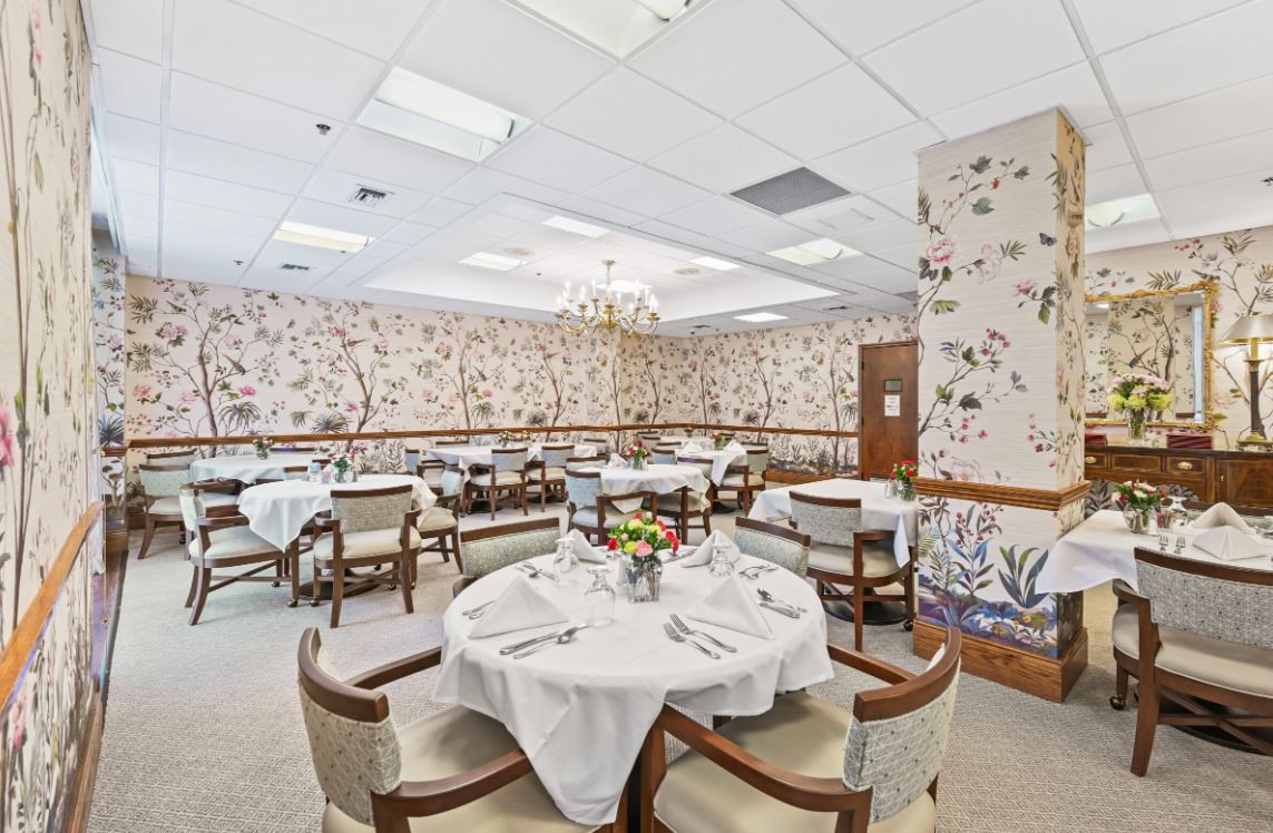An elegant dining room with floral wallpaper, chandeliers, and neatly set tables.