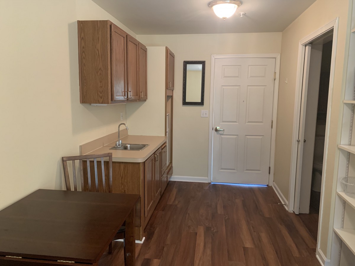 A small kitchen area with wooden cabinets, a sink, and a dining table set on a wooden floor.