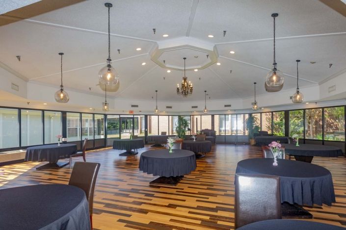 An elegant banquet hall with modern lighting, round tables, and a wooden floor.