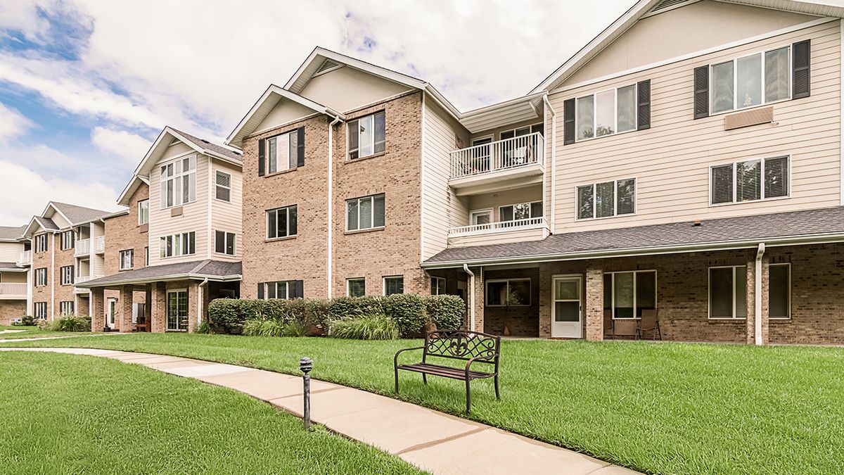 A residential apartment building with a well-maintained lawn and a bench along the pathway.