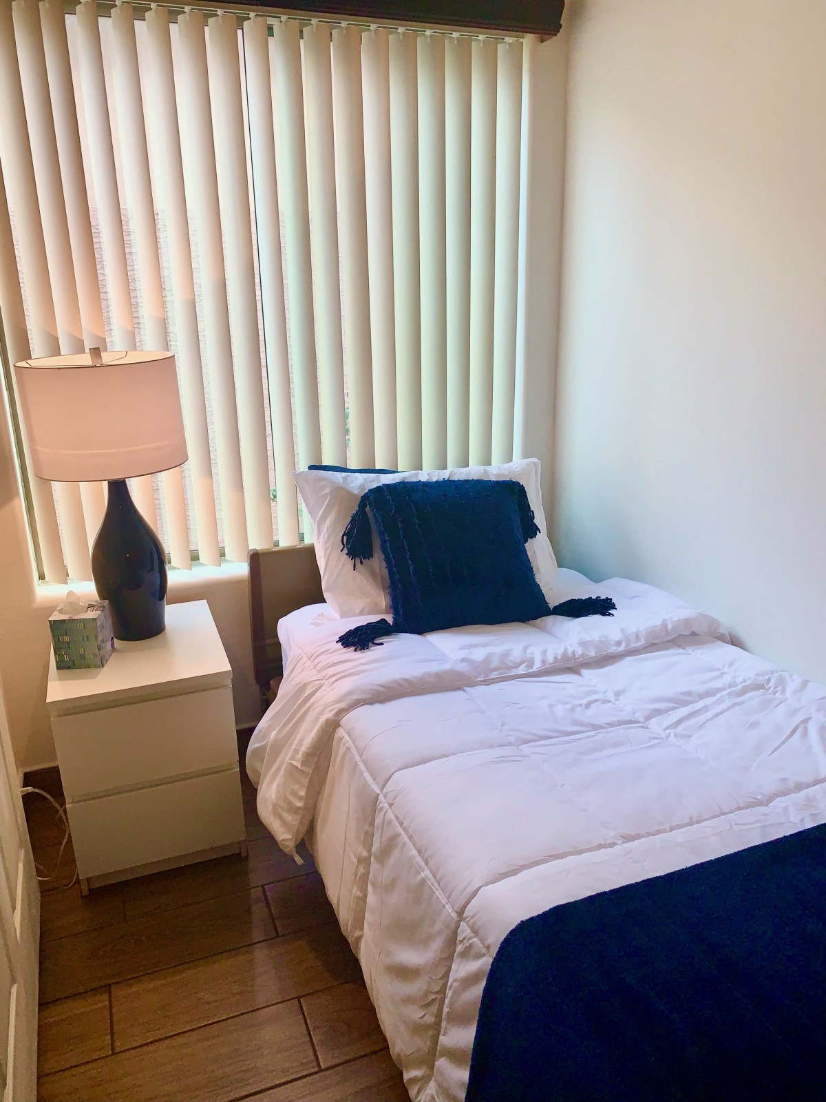 A minimalist bedroom with a single bed, nightstand, and lamp by the window.
