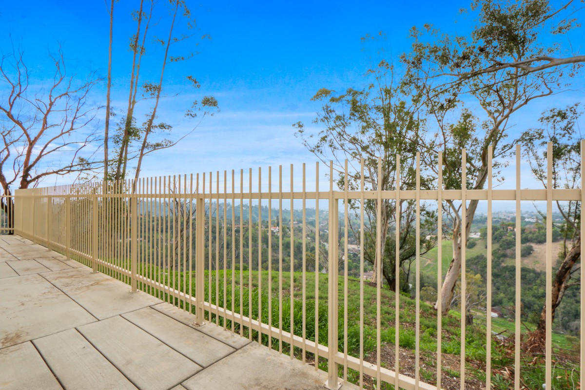 A scenic outdoor view with a metal fence overlooking a lush landscape and clear blue sky.