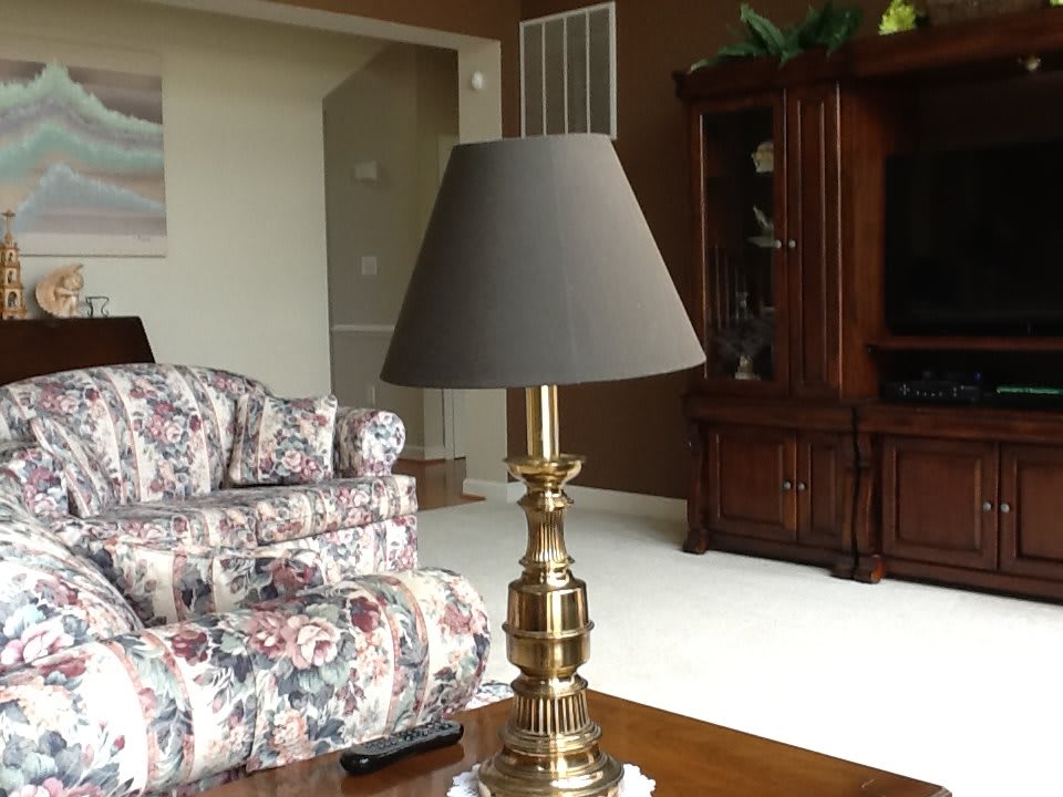 A traditional living room setting featuring a brass lamp with a dark shade next to a floral-patterned couch.