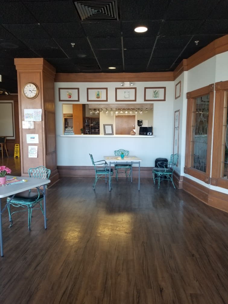 An empty cafe interior with wooden floors, tables, and chairs, decorated with artwork on the walls.