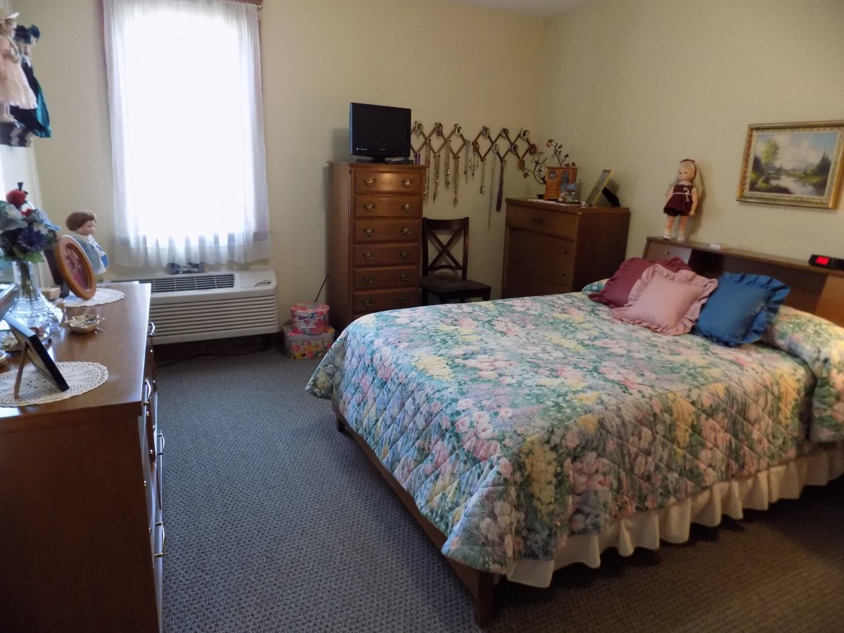 A cozy bedroom featuring a bed with a floral bedspread, dressers, and various decorations.