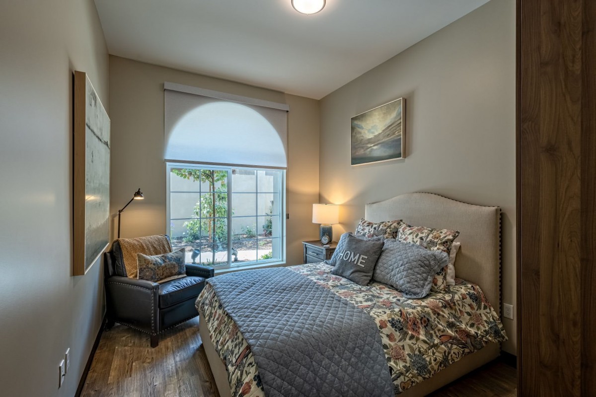 A cozy bedroom with a large window, featuring a neatly made bed and comfortable chair.