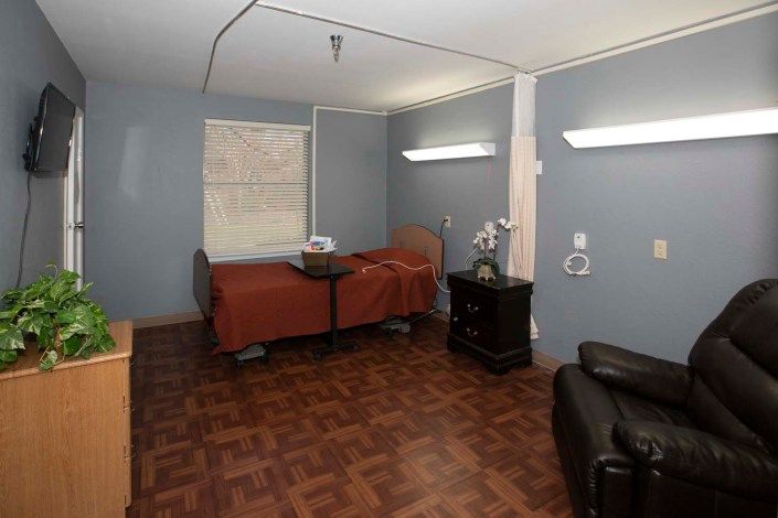 A hospital room with a single patient bed, chair, and medical equipment.
