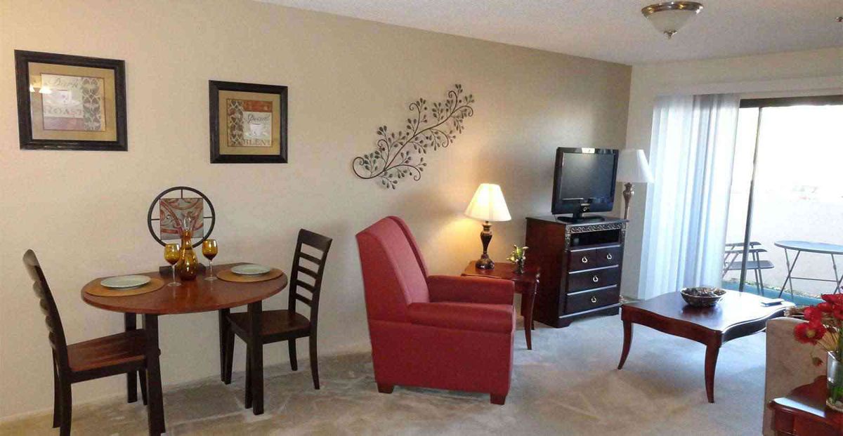 A cozy living room with a red armchair, wall art, a TV, and a small dining table set.