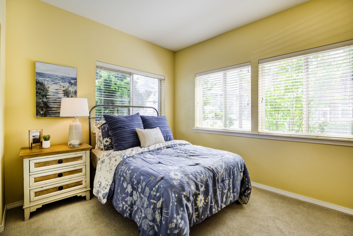 A cozy bedroom with a neatly made bed and ample natural light from multiple windows.