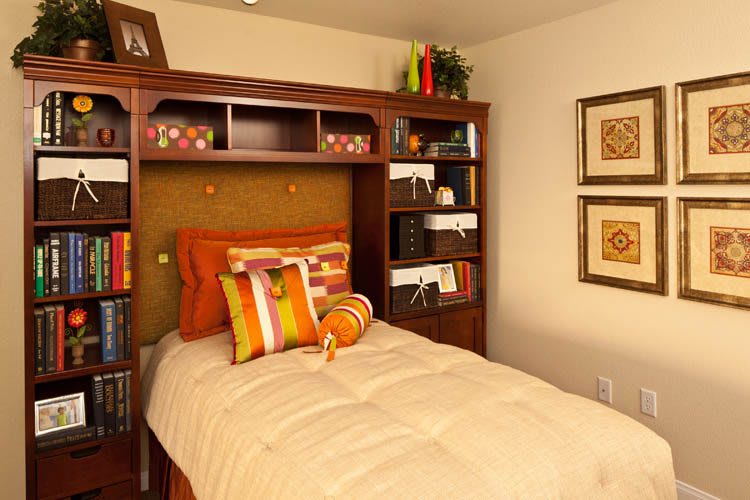 A cozy bedroom with a single bed and wooden shelves adorned with decorative orange pillows and wall art.
