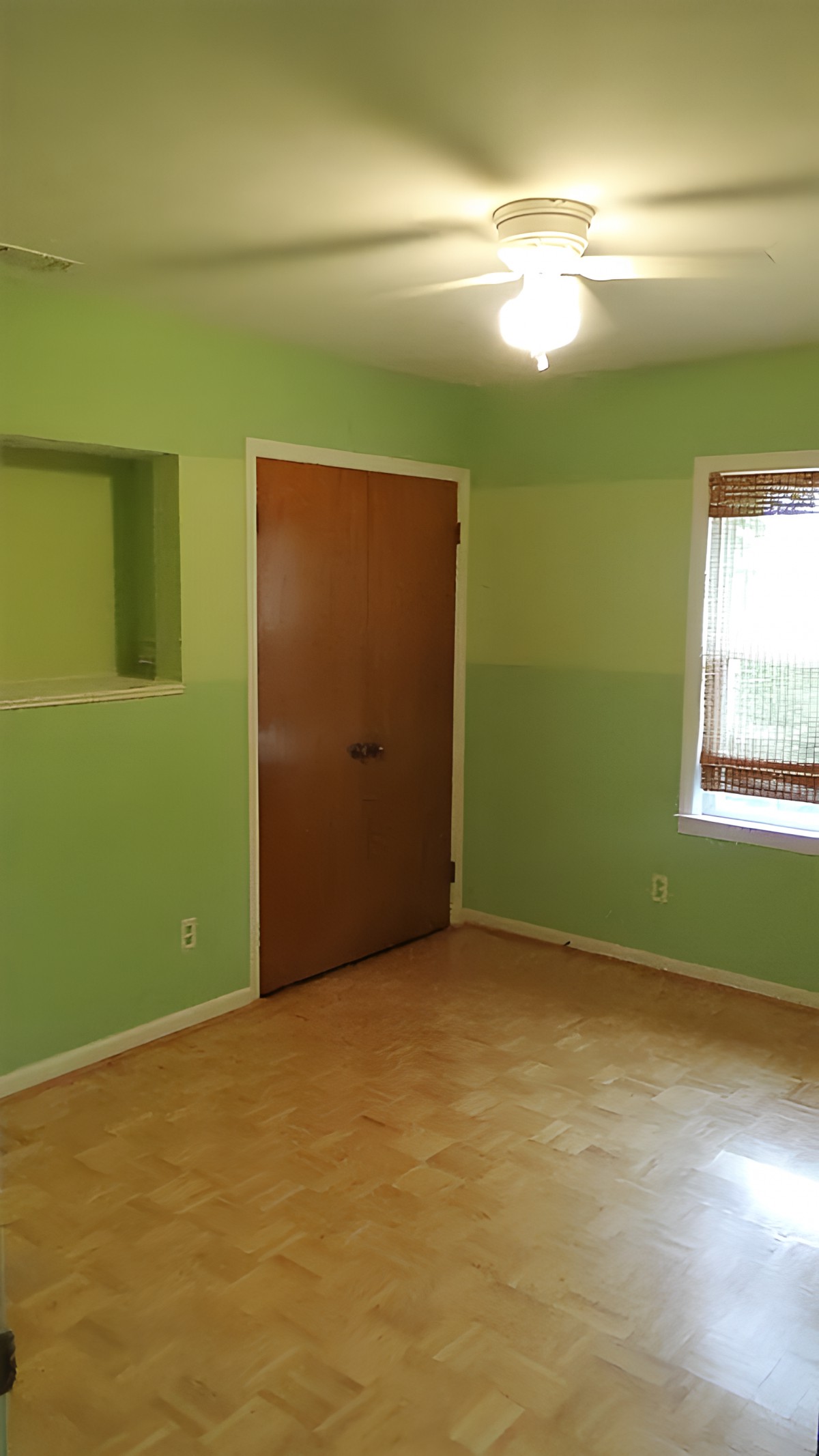 An empty room with green walls, a wooden door, and a window with bamboo blinds.