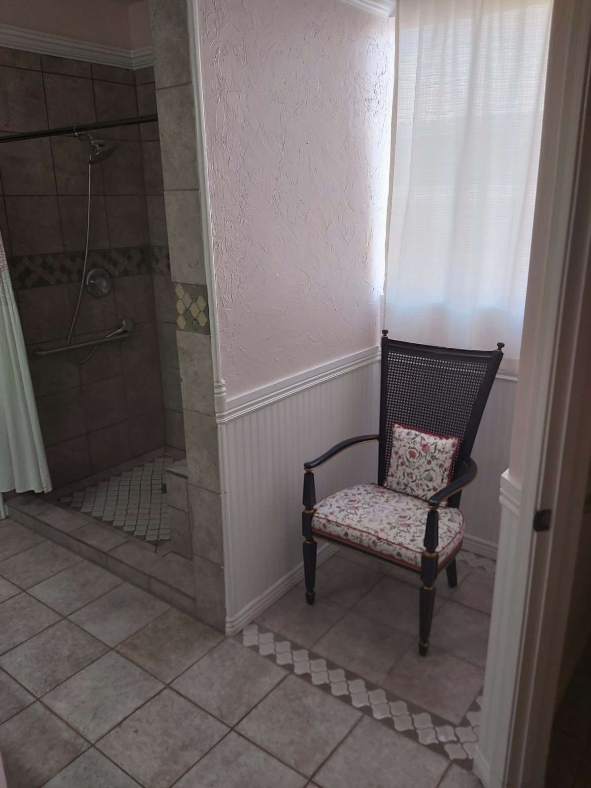 A bathroom interior featuring a chair next to a tiled shower area.