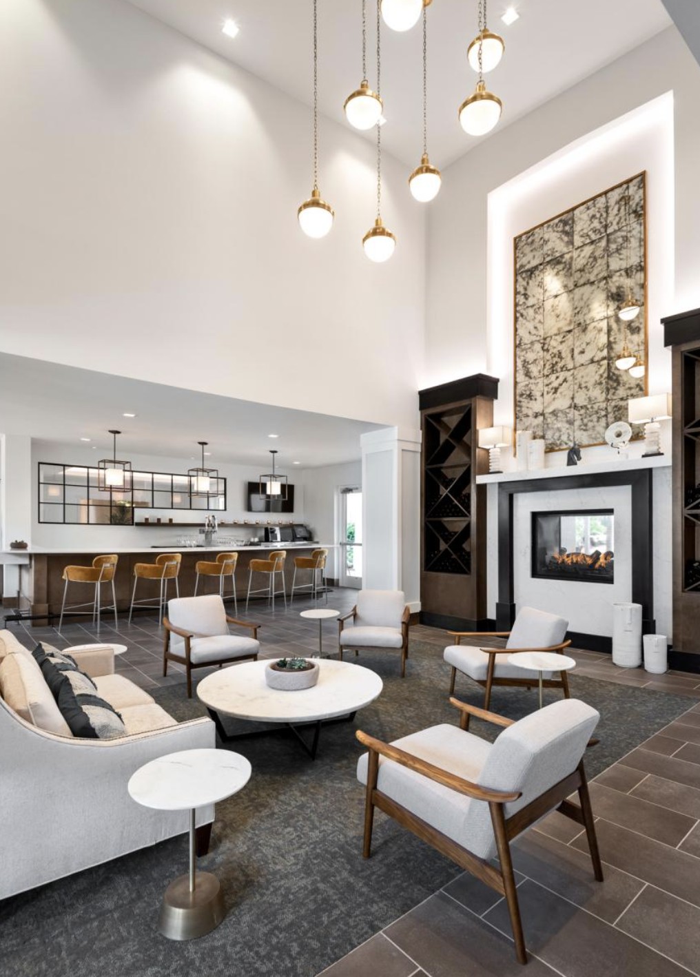 A modern living room with an open seating area, featuring a high ceiling, chandelier lighting, and a stylish bar counter.