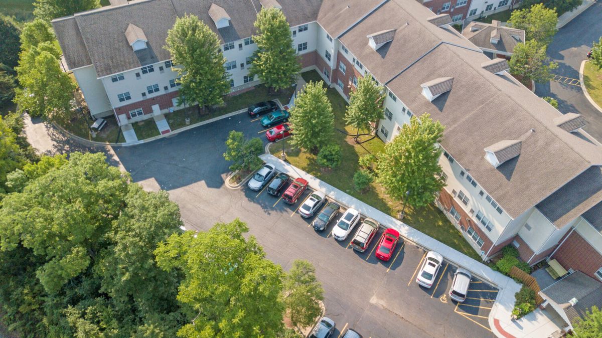 Aerial view of a residential building with a parking lot surrounded by trees.