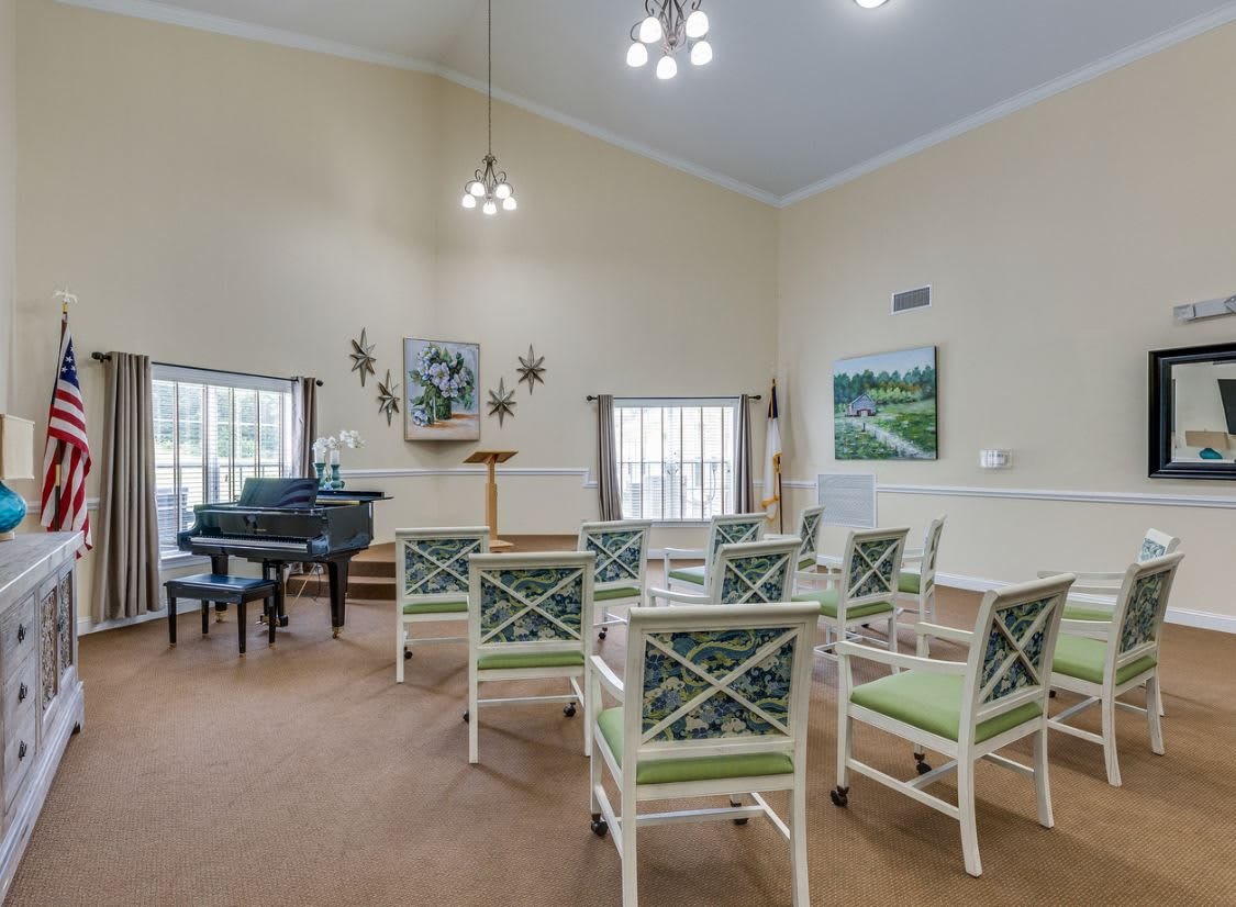 A well-lit meeting room with a grand piano, surrounded by green cushioned chairs and decorated with artwork on the walls.