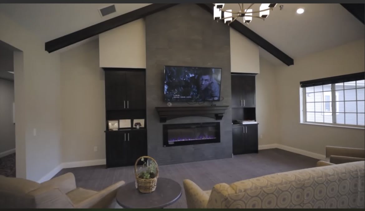 A modern living room with a vaulted ceiling, featuring a large television mounted above a sleek fireplace and surrounded by dark cabinetry.