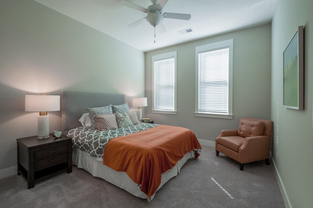 Cozy bedroom with a comfortable bed, stylish lamp, and armchair by the window.