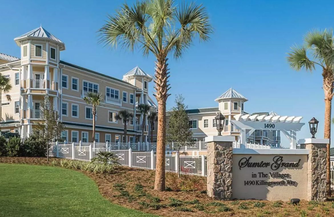 A resort building with a palm tree in the foreground and a welcoming sign.