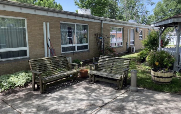 Outdoor seating area with wooden benches and a brick building in the background.
