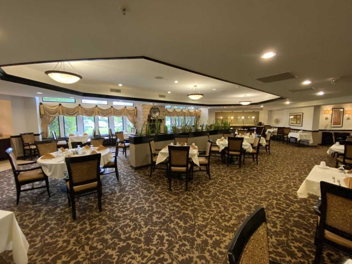 An elegant dining area with neatly arranged tables and chairs, featuring a carpeted floor and large windows.