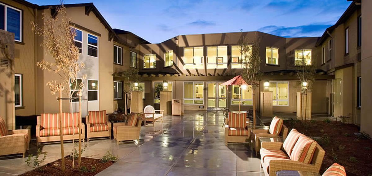 A cozy courtyard with outdoor seating in front of a well-lit residential building during the evening.