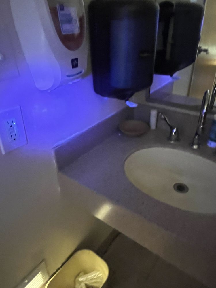 A bathroom sink area illuminated with blue light, featuring a mirror, hand dryer, and soap dispenser.