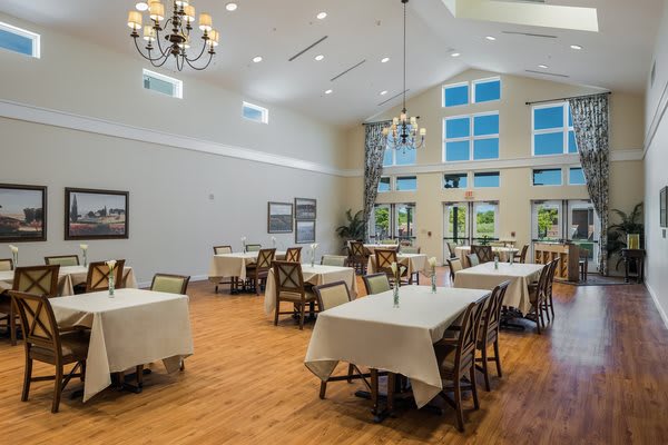 A spacious dining room with elegant chandeliers, large windows, and neatly arranged tables.