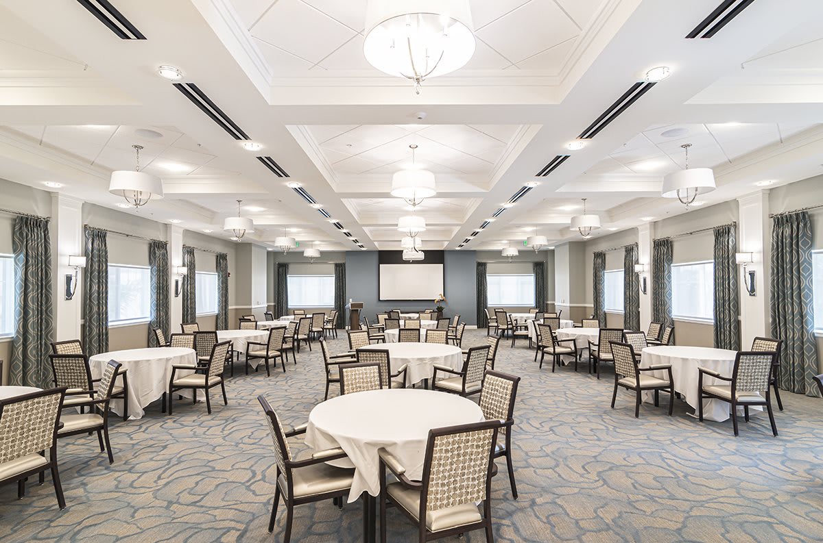 A spacious banquet hall with round tables and chairs, well-lit and ready for an event.