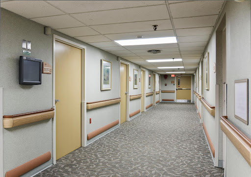 A view of a well-lit healthcare hallway with closed doors and carpeted flooring.