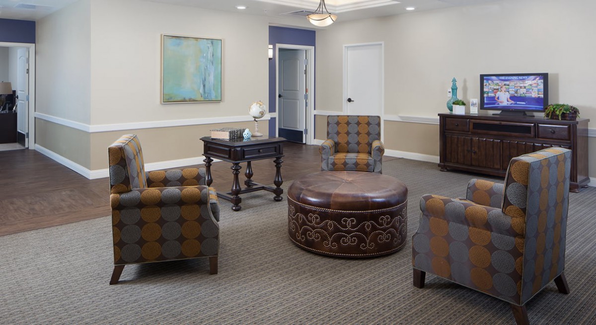 A cozy lounge area featuring comfortable seating with patterned chairs and a central round ottoman, complemented by artwork and decorative pieces.
