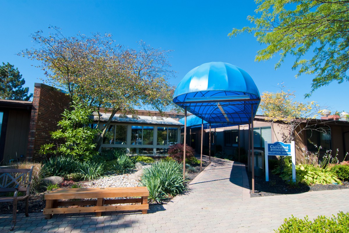The entrance of a building with a blue canopy and landscaped surroundings.