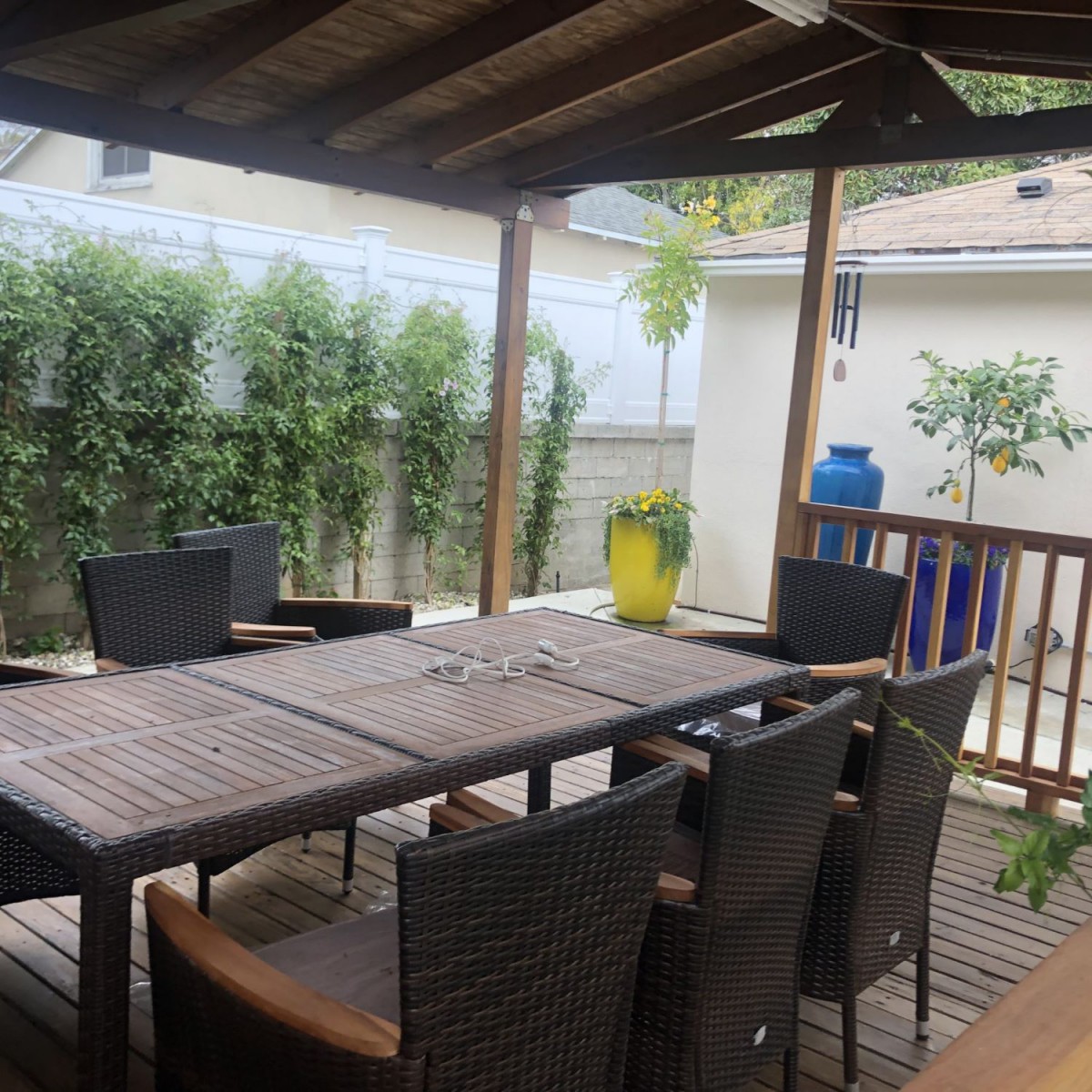 A covered outdoor patio with a dining table and chairs, surrounded by greenery.