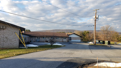 A peaceful view of a residential building with a backdrop of rolling hills and cloudy sky.