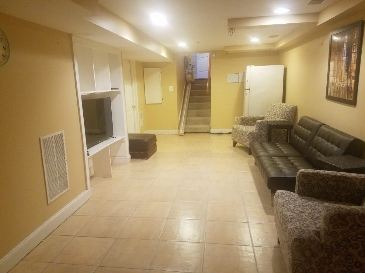 A spacious basement living area with a sofa, television, and tiled flooring.