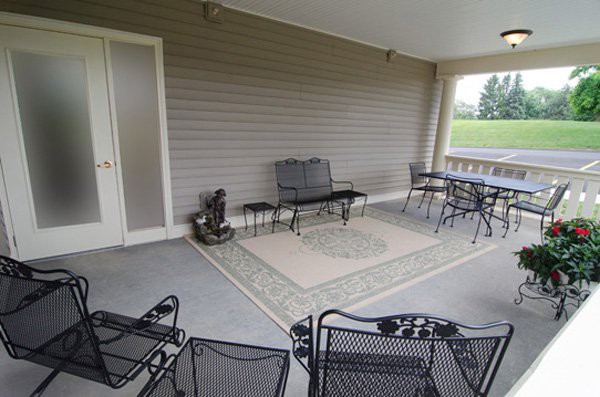 A covered patio with outdoor furniture, including metal chairs and a table on an area rug.