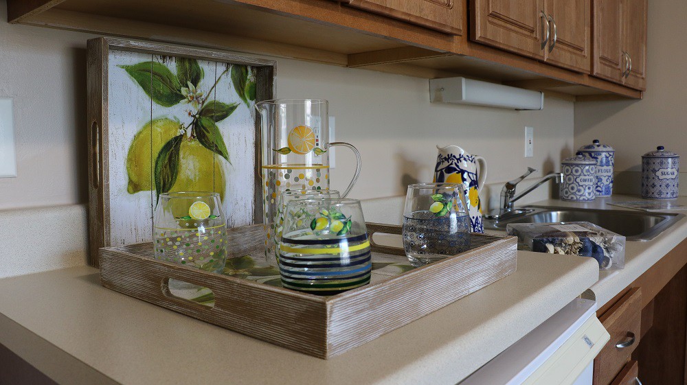 A decorated kitchen countertop featuring a wooden tray with glassware, a lemon-themed decor, and a candle holder.