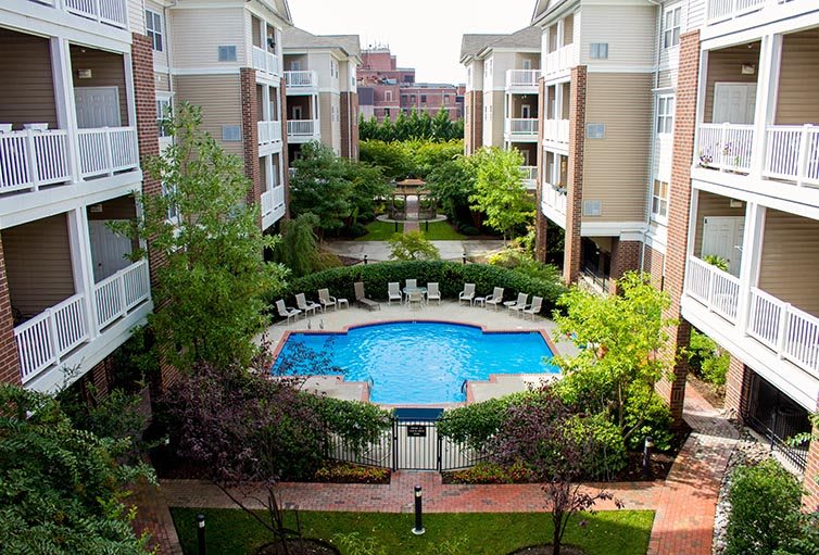 A view of an apartment complex courtyard featuring a swimming pool surrounded by greenery and residential buildings.