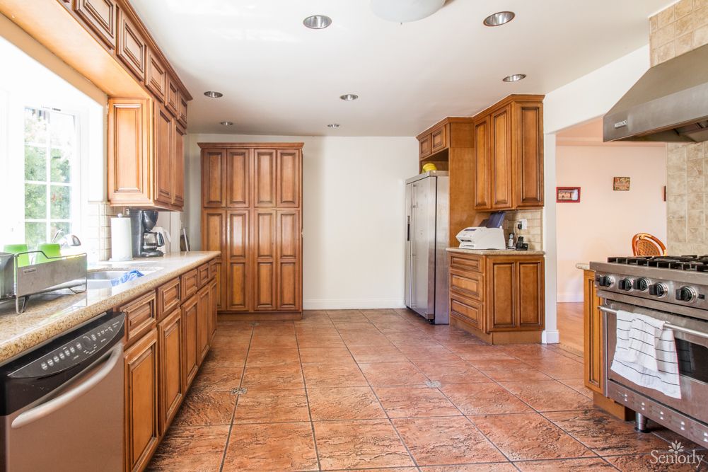 A spacious kitchen with wood cabinets and a tile floor, featuring stainless steel appliances.
