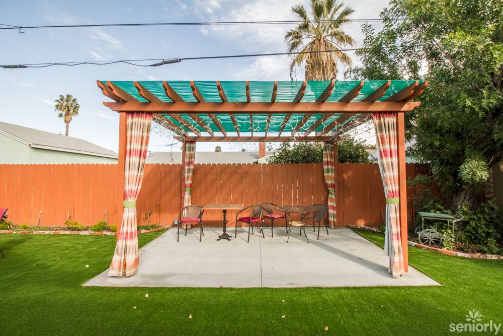 A backyard pergola providing shade over a patio area with outdoor furniture.
