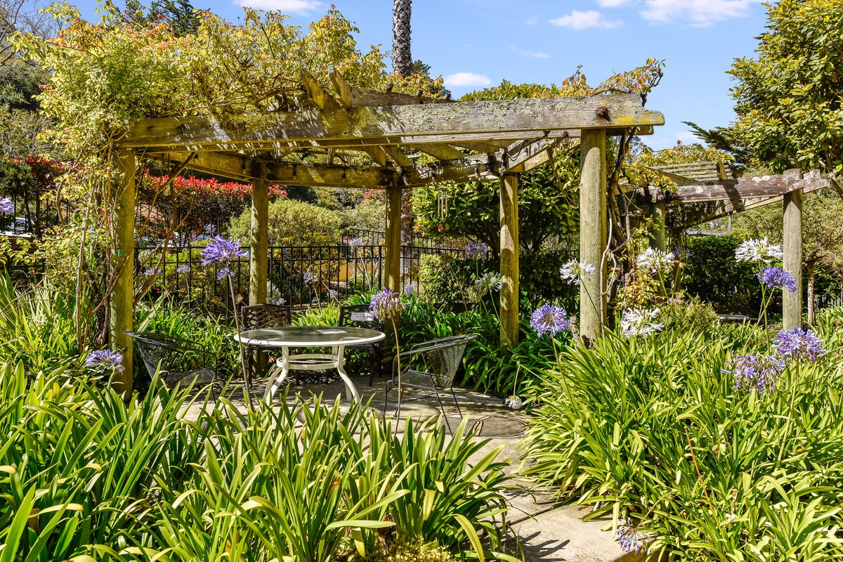A tranquil garden setting featuring a pergola and outdoor seating surrounded by lush greenery and flowers.