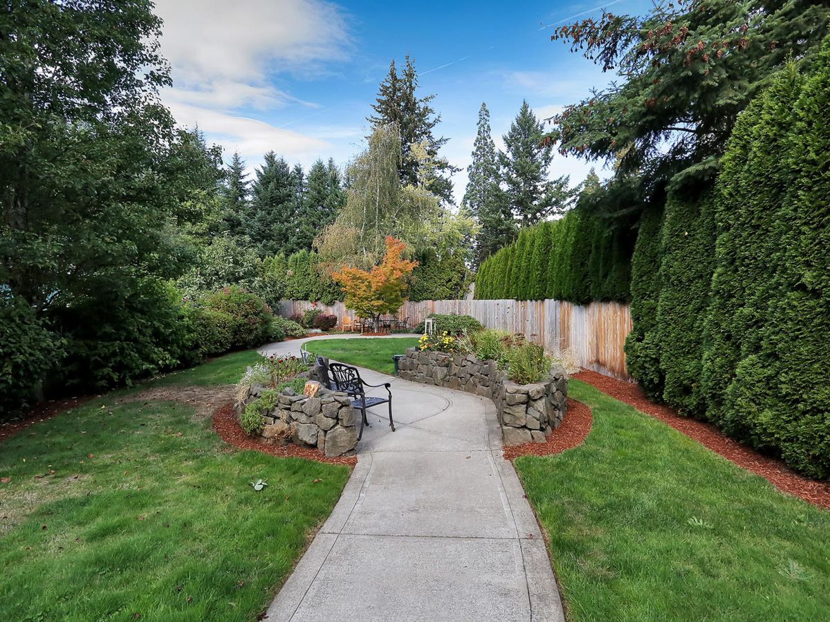 A scenic garden pathway with a bench surrounded by lush greenery and trees.
