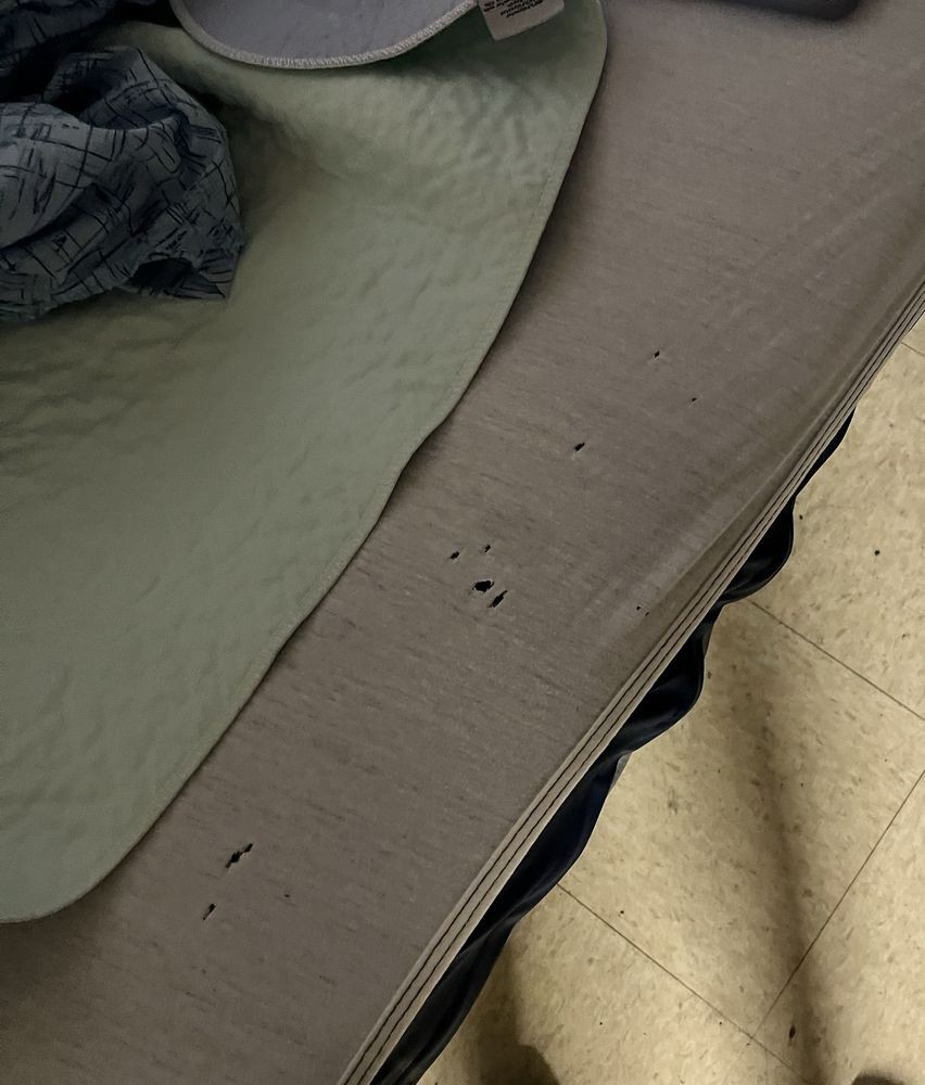 A bedsheet with multiple holes lies on a bed beside a tiled floor.