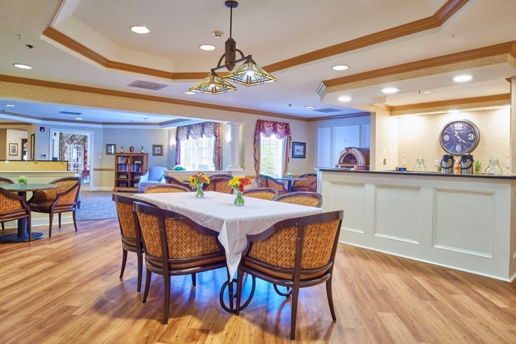 A cozy dining room with a table set for four, featuring wicker chairs and elegant lighting.