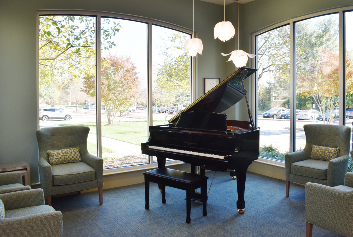 A grand piano elegantly placed in a sunlit living room with large windows and comfortable seating.