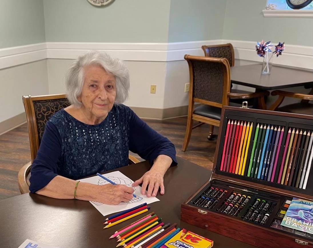 An elderly woman engaging in a drawing activity with colored pencils at a table.