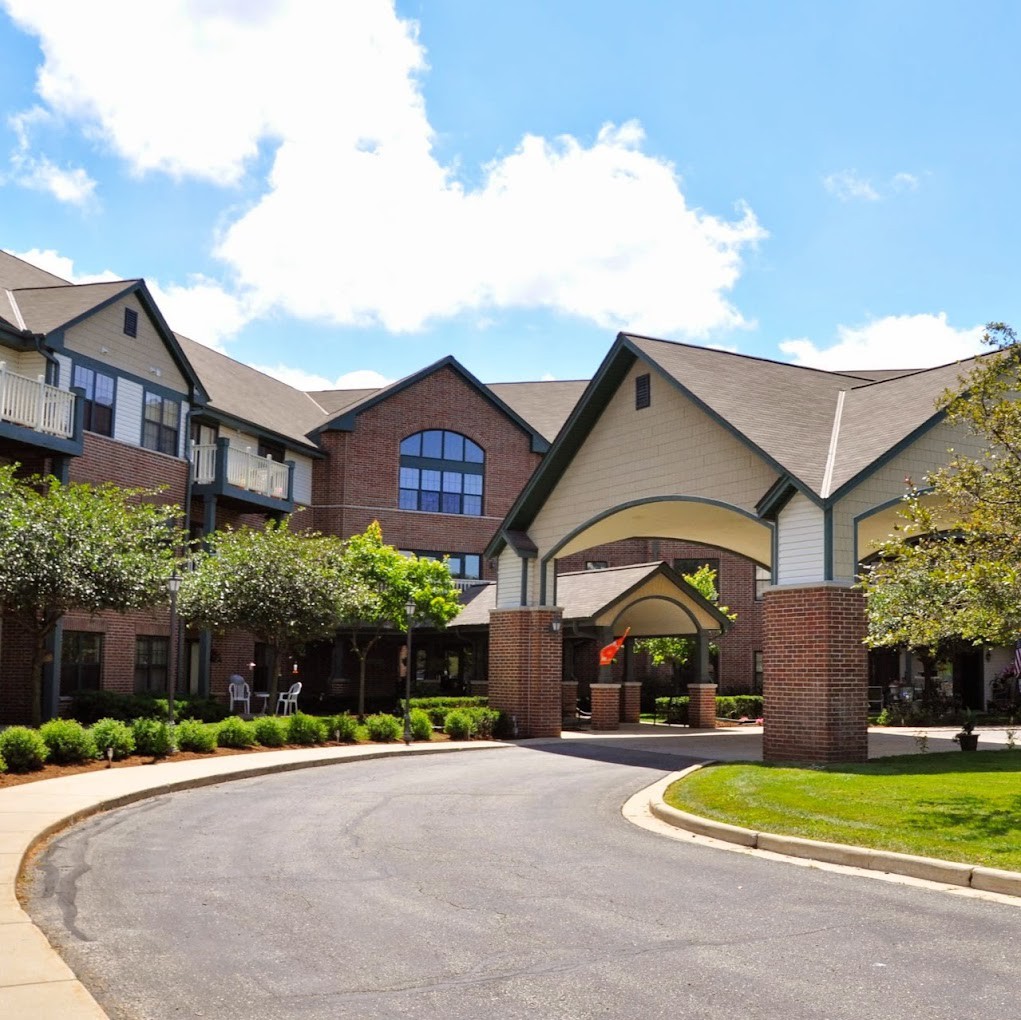 A large residential building with a curved driveway and manicured landscaping under a partly cloudy sky.