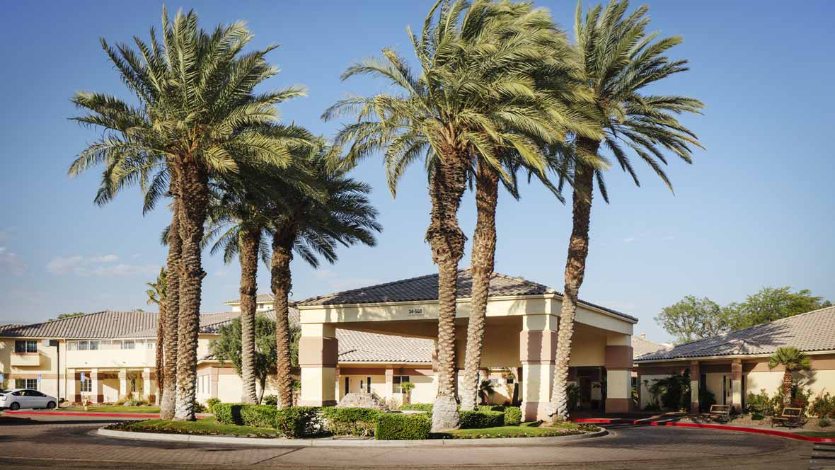 A hotel building surrounded by palm trees under a clear blue sky.