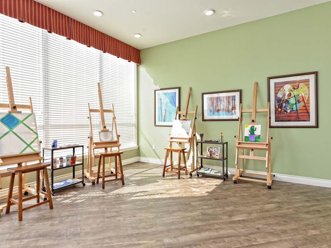 A well-lit art studio featuring several easels and paintings displayed on the walls.
